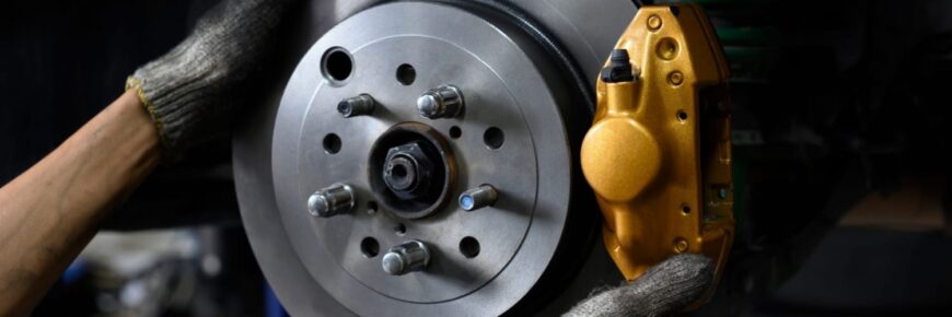Automotive Repair & Tire Shop Oakville, ON - Sil’s Auto Care Centre Close-up of a person wearing gloves working on a car brake system, showing a metallic brake disc and gold-coloured calliper during brake and rotor replacement. | Call Us Today At +1 (905) 823-2626