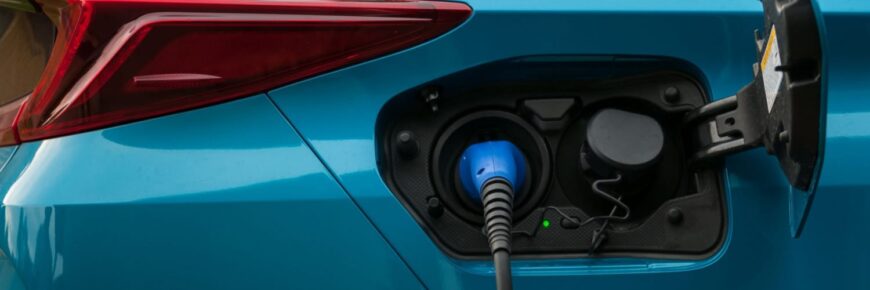 Automotive Repair & Tire Shop Oakville, ON - Sil’s Auto Care Centre Close-up of an electric vehicle being charged, with the cable plugged into the port on a blue car—perfect for illustrating Hybrid Repair services. The taillight and charging hatch are also visible. | Call Us Today At +1 (905) 823-2626