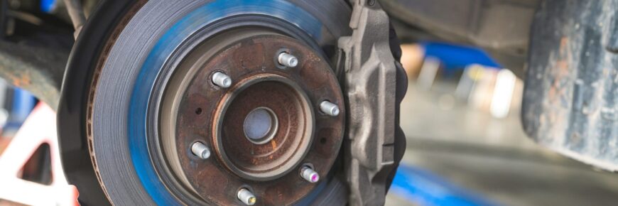Automotive Repair & Tire Shop Oakville, ON - Sil’s Auto Care Centre Close-up of a car’s exposed brake disc and calliper at a brake shop, showing the metal rotor, wheel studs, and some rust on the hub. The wheel has been removed for maintenance or repair. | Call Us Today At +1 (905) 823-2626