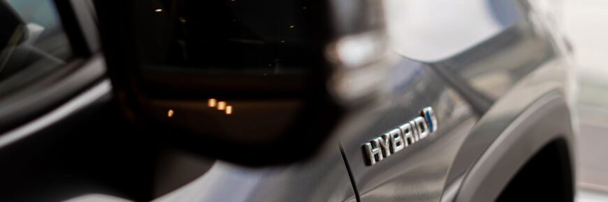 Automotive Repair & Tire Shop Oakville, ON - Sil’s Auto Care Centre Close-up of a car’s side with a metallic HYBRID badge visible, hinting at advanced Hybrid Battery Service; part of the vehicle’s wing mirror and blurred reflections are seen on the sleek body. | Call Us Today At +1 (905) 823-2626