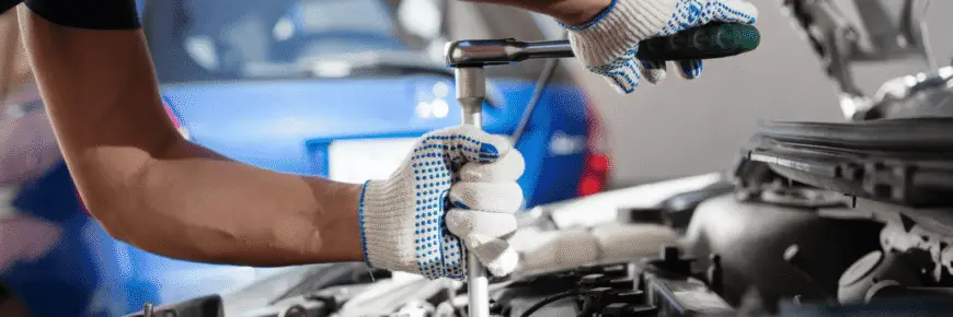 Automotive Repair & Tire Shop Oakville, ON - Sil’s Auto Care Centre A person wearing white work gloves uses a ratchet spanner to work on a car engine, with a blue car in the blurred background—capturing the attention of anyone searching for "Car Repair Near Me. | Call Us Today At +1 (905) 823-2626