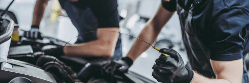 Automotive Repair & Tire Shop Oakville, ON - Sil’s Auto Care Centre Two mechanics wearing black gloves work on a car engine at a Garage Near Me. One checks the engine with a dipstick while the other leans over the bay, both focused on vehicle maintenance. | Call Us Today At +1 (905) 823-2626