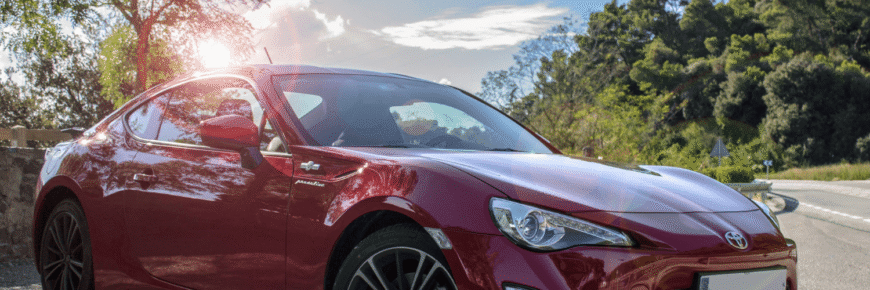 Automotive Repair & Tire Shop Oakville, ON - Sil’s Auto Care Centre A shiny red Toyota sports car parked by a roadside, sunlight reflecting off the bonnet, powered by a reliable Toyota battery, with trees and blue sky in the background. | Call Us Today At +1 (905) 823-2626