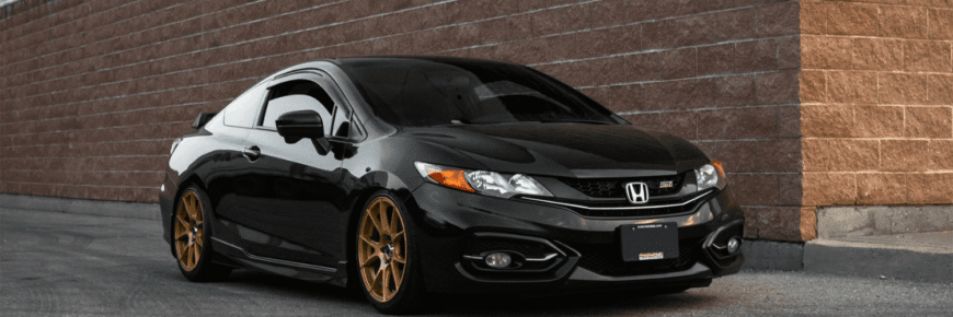 Automotive Repair & Tire Shop Oakville, ON - Sil’s Auto Care Centre A black Honda Civic coupé with tinted windows and bronze aftermarket wheels, freshly maintained with a Honda A1 service, is parked next to a brick wall on a paved surface. | Call Us Today At +1 (905) 823-2626