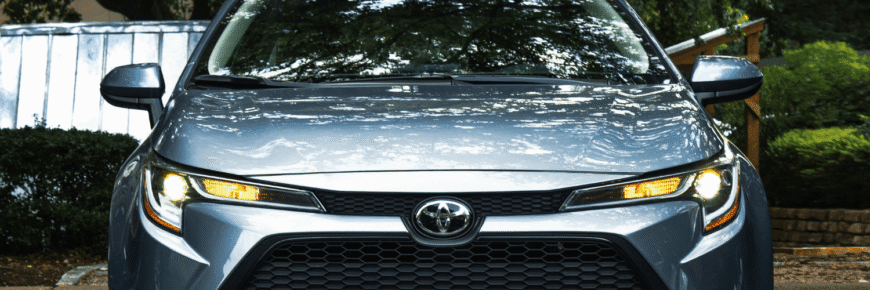 Automotive Repair & Tire Shop Oakville, ON - Sil’s Auto Care Centre A silver Toyota saloon is parked outdoors, shown from the front with headlights on. Trees and greenery are reflected on the windscreen, creating a fresh look—perfect for showcasing your next Toyota oil change. | Call Us Today At +1 (905) 823-2626