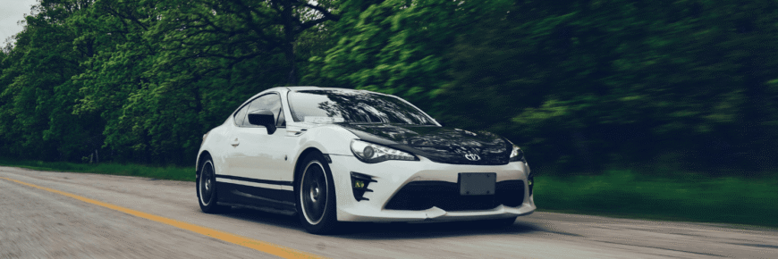 Automotive Repair & Tire Shop Oakville, ON - Sil’s Auto Care Centre A white sports car with black accents drives on a road lined with green trees, moving quickly as the background blurs—ensuring peak performance thanks to regular Toyota Scheduled Maintenance. | Call Us Today At +1 (905) 823-2626