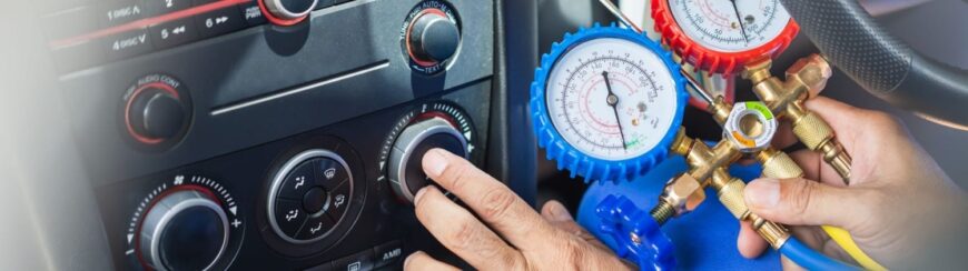 Automotive Repair & Tire Shop Oakville, ON - Sil’s Auto Care Centre A person adjusts car air conditioning controls while holding a set of HVAC manifold gauges with blue and red dials, inspecting or servicing the vehicle’s air conditioning system. | Call Us Today At +1 (905) 823-2626