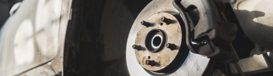 Automotive Repair & Tire Shop Oakville, ON - Sil’s Auto Care Centre Close-up of a car brake disc and calliper with the wheel removed, showing the metal surface and wheel studs, in a well-lit garage or workshop setting. | Call Us Today At +1 (905) 823-2626