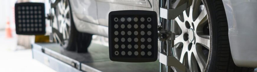 Automotive Repair & Tire Shop Oakville, ON - Sil’s Auto Care Centre Close-up of a car undergoing wheel alignment, with alignment sensors attached to the front wheels on a platform in a car repair shop. | Call Us Today At +1 (905) 823-2626