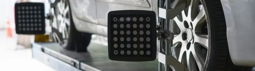 Automotive Repair & Tire Shop Oakville, ON - Sil’s Auto Care Centre Close-up of a car undergoing wheel alignment, with alignment sensors attached to the front wheels on a platform in a car repair shop. | Call Us Today At +1 (905) 823-2626