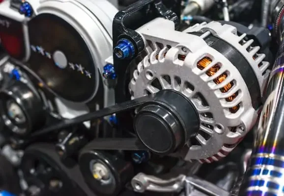 Automotive Repair & Tire Shop Oakville, ON - Sil’s Auto Care Centre Close-up of a car engine with a visible alternator, belts, and metal components. The alternator’s copper coils and pulley are prominently shown, with other engine parts and wires surrounding it. | Call Us Today At +1 (905) 823-2626