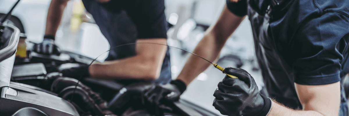 Automotive Repair & Tire Shop Oakville, ON - Sil’s Auto Care Centre Two mechanics wearing black gloves work on a car engine at a Garage Near Me. One checks the engine with a dipstick while the other leans over the bay, both focused on vehicle maintenance. | Call Us Today At +1 (905) 823-2626