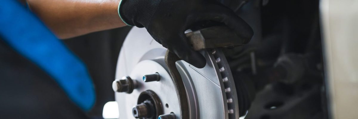Automotive Repair & Tire Shop Oakville, ON - Sil’s Auto Care Centre A person wearing black gloves is installing or inspecting a brake pad and disc on a vehicle’s wheel assembly, showcasing professional Brake Repair Mississauga services. | Call Us Today At +1 (905) 823-2626