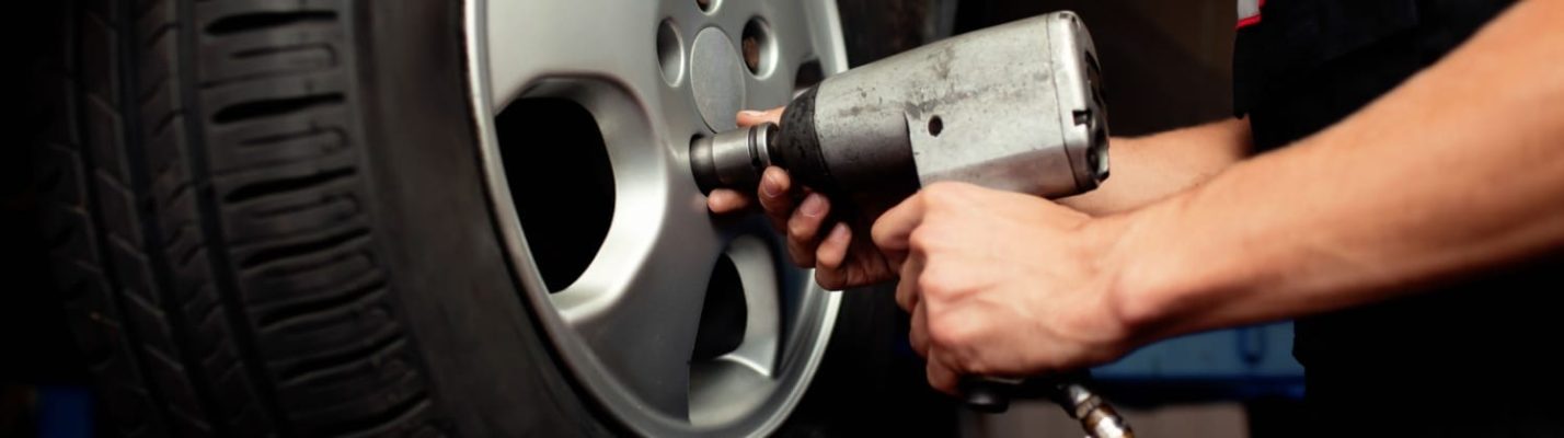 Automotive Repair & Tire Shop Oakville, ON - Sil’s Auto Care Centre A person uses a power tool to tighten or loosen the wheel nuts on a car wheel, preparing for tyre removal or installation in a car repair setting. | Call Us Today At +1 (905) 823-2626