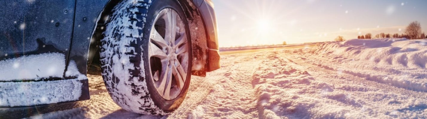 Automotive Repair & Tire Shop Oakville, ON - Sil’s Auto Care Centre Close-up of a car tyre driving on a snow-covered road in bright sunlight, with snowbanks on the sides and a clear sky in the background. | Call Us Today At +1 (905) 823-2626