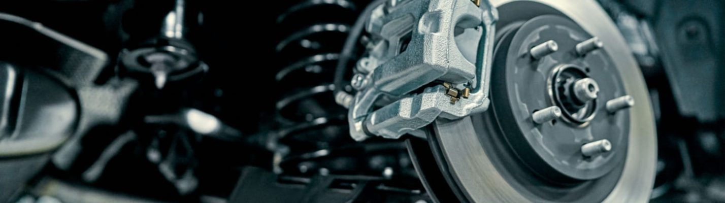 Automotive Repair & Tire Shop Oakville, ON - Sil’s Auto Care Centre Close-up view of a car’s disc brake assembly, showing the brake calliper mounted on the metal rotor with suspension components visible in the background. | Call Us Today At +1 (905) 823-2626