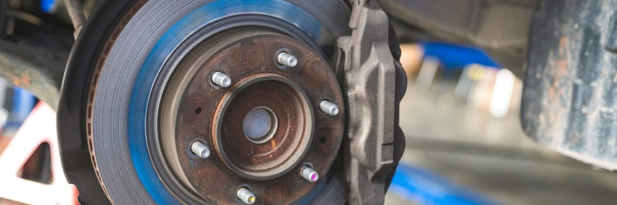 Automotive Repair & Tire Shop Oakville, ON - Sil’s Auto Care Centre Close-up of a car’s exposed brake disc and calliper at a brake shop, showing the metal rotor, wheel studs, and some rust on the hub. The wheel has been removed for maintenance or repair. | Call Us Today At +1 (905) 823-2626