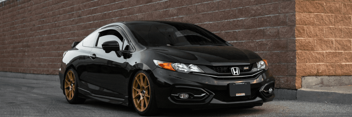 Automotive Repair & Tire Shop Oakville, ON - Sil’s Auto Care Centre A black Honda Civic coupé with tinted windows and bronze aftermarket wheels, freshly maintained with a Honda A1 service, is parked next to a brick wall on a paved surface. | Call Us Today At +1 (905) 823-2626