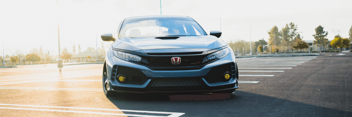 Automotive Repair & Tire Shop Oakville, ON - Sil’s Auto Care Centre A grey Honda Civic with yellow fog lights is parked in an empty car park on a sunny day, facing the camera. Trees and lamp posts are visible in the background—perfect for anyone searching “Honda Mechanic Near Me.”. | Call Us Today At +1 (905) 823-2626