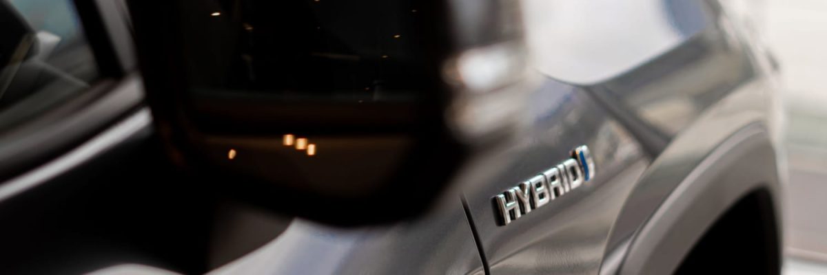Automotive Repair & Tire Shop Oakville, ON - Sil’s Auto Care Centre Close-up of a car’s side with a metallic HYBRID badge visible, hinting at advanced Hybrid Battery Service; part of the vehicle’s wing mirror and blurred reflections are seen on the sleek body. | Call Us Today At +1 (905) 823-2626