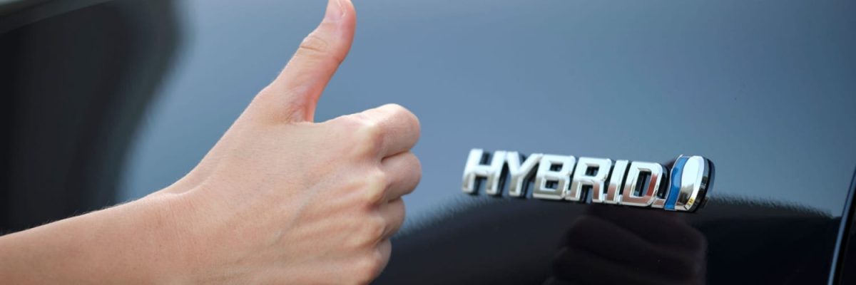 Automotive Repair & Tire Shop Oakville, ON - Sil’s Auto Care Centre A hand giving a thumbs-up next to the chrome HYBRID badge on a shiny black car, signalling satisfaction with hybrid car maintenance. | Call Us Today At +1 (905) 823-2626
